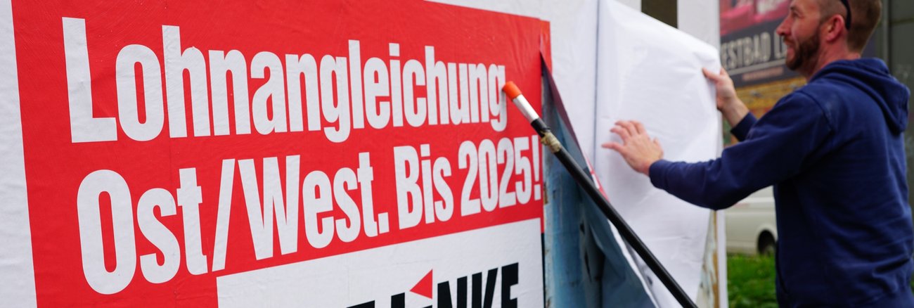 Ein Arbeiter bringt am 2. Mai 2019 in Leipzig eine Großfläche an mit der Aufschrift: »1:1 - Lohnangleichung Ost/West. Bis 2025!« © Olaf Krostiz