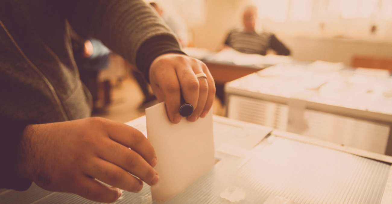 Mann in Wahllokal steckt seinen Stimmzettel in eine Wahlurne © iStock/bizoo_n