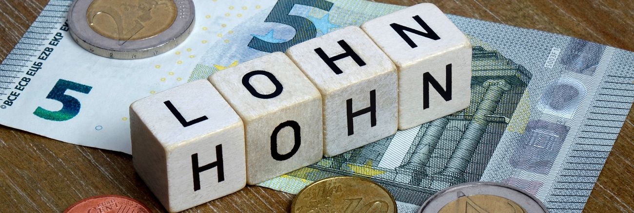 Auf einem Fünf-Euro-Schein stehen Würfel mit den Worten Lohn und Hohn © picture alliance/dpa-Zentralbild