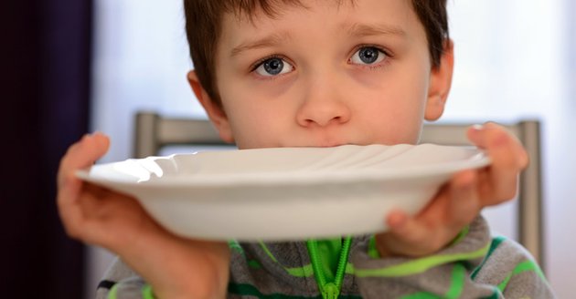 Ein Junge hält einen Teller vor seinen Mund © iStockphoto/djedzura