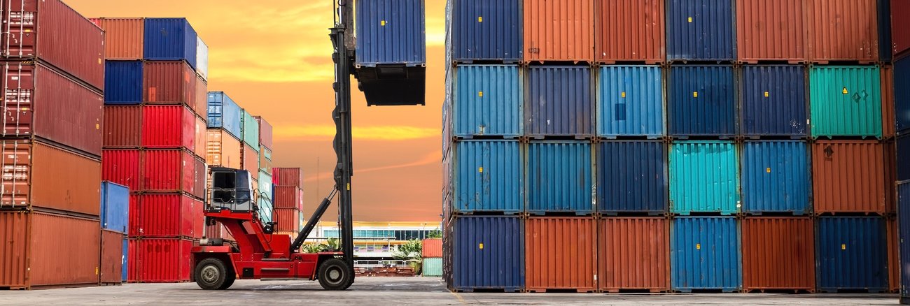 Ein roter Gabelstapler vor einem hohen Containerstapel © iStock/bugphai