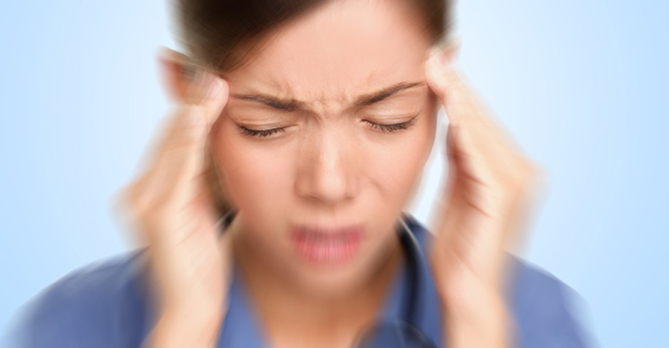 Frau in blauem Hemd fasst sich mit den Fingern beider Hände an die Schläfen und zieht mit geschlossenen Augen die Augenbrauen zusammen. | © iStockphoto.com/Maridav