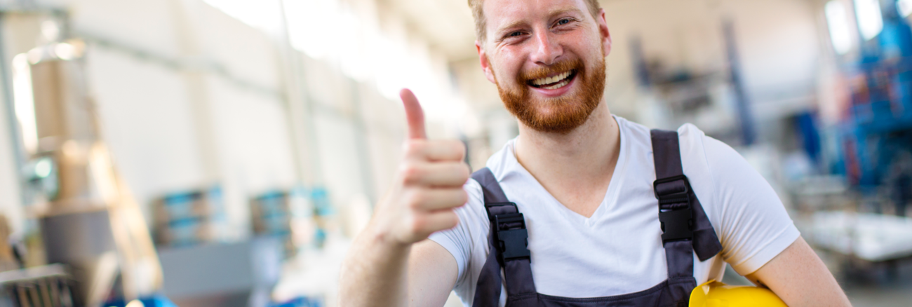 Ein Arbeiter mit gelbem Helm unter seinem linken Arm hebt zustimmend den rechten Daumen © iStock/milanvirijevic