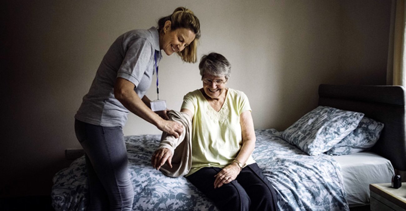 Eine Pflegerin hilft einer älteren Frau beim Anziehen © iStockphoto.com/SolStock