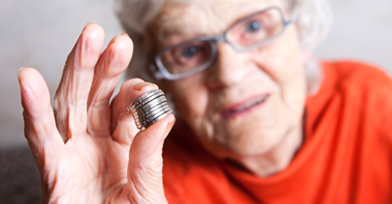 Eine ältere Frau hält Euro-Münzen zwischen Daumen und Zeigefinger © iStock/Rendery