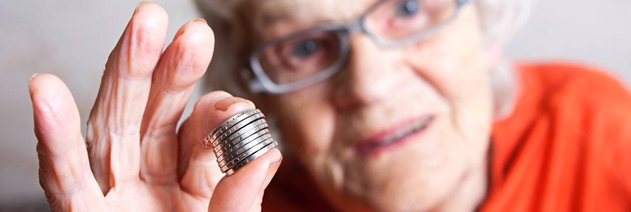 Eine ältere Frau hält Euro-Münzen zwischen Daumen und Zeigefinger © iStock/Rendery