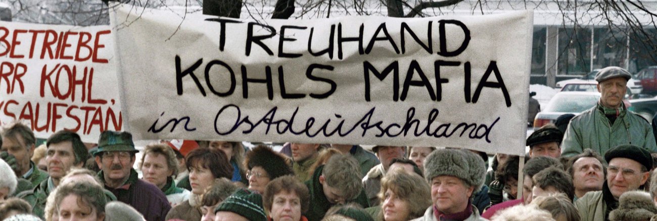 Bei einer Demonstration gegen die Treuhandanstalt im Jahre 1991 am Alexanderplatz in Berlin halten Teilnehmer ein Transparent mit der AUfschrift: Treuhand Kohls Mafia in Ostdeutschland © dpa/Paul Glaser