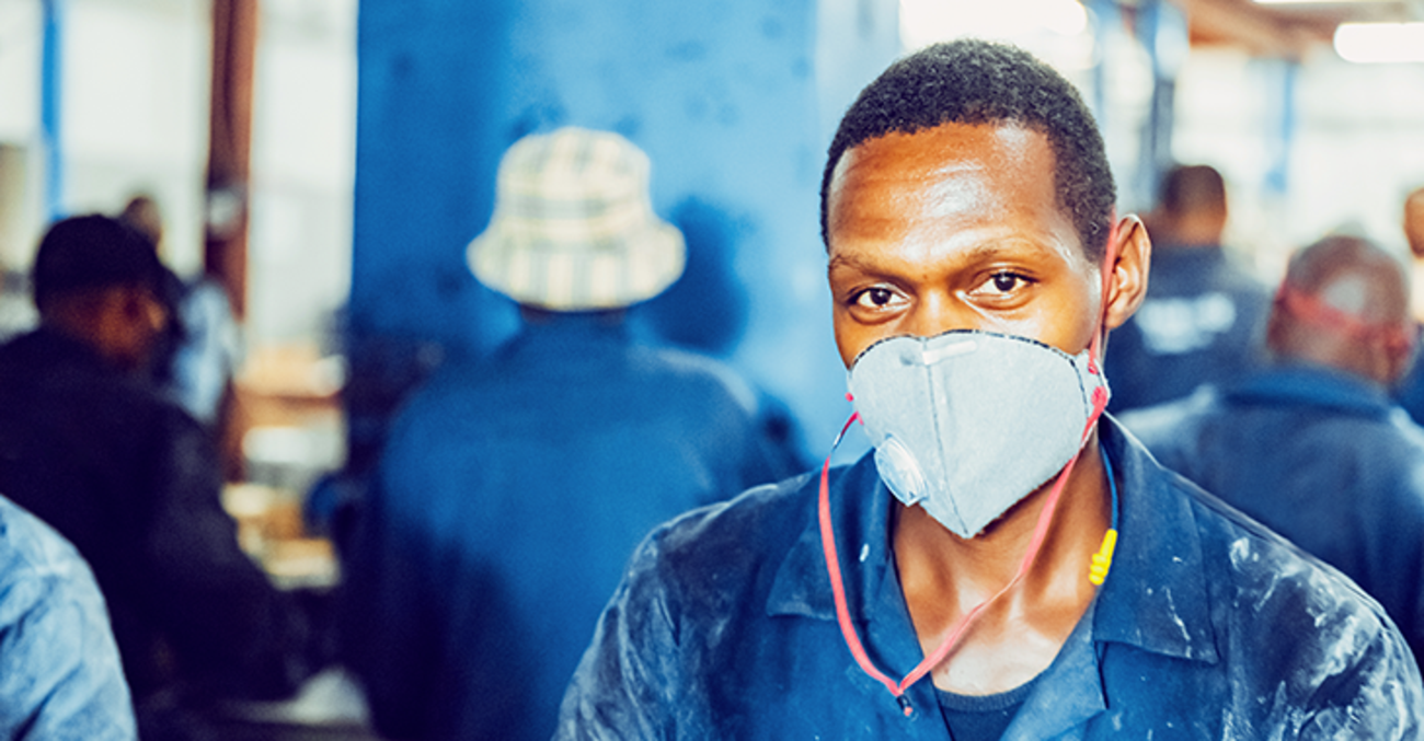 Afrikanischer Arbeiter in blauer Arbeitskleidung mit Atemschutzmaske und Gehörschutz in einer Fabrik | Foto: © istock.com/GCShutter
