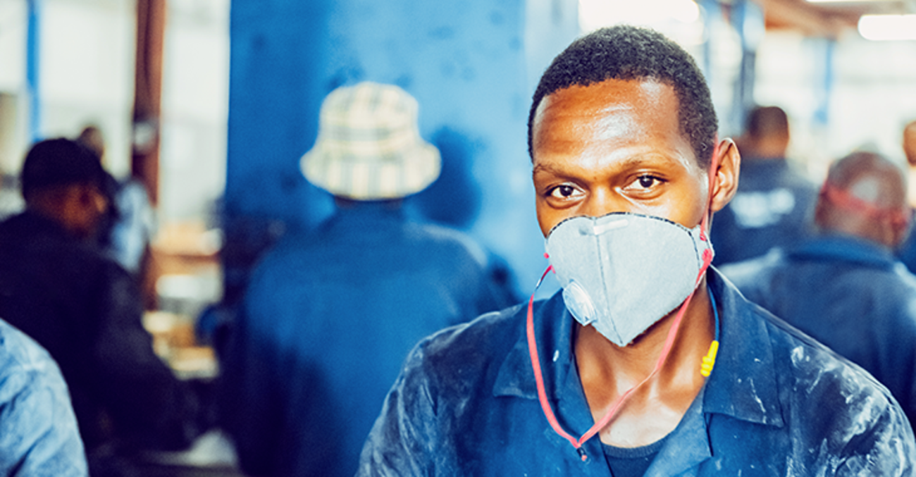 Afrikanischer Arbeiter in blauer Arbeitskleidung mit Atemschutzmaske und Gehörschutz in einer Fabrik | Foto: © istock.com/GCShutter Afrikanischer Arbeiter in blauer Arbeitskleidung mit Atemschutzmaske und Gehörschutz in einer Fabrik | Foto: © istock.com/GCShutter