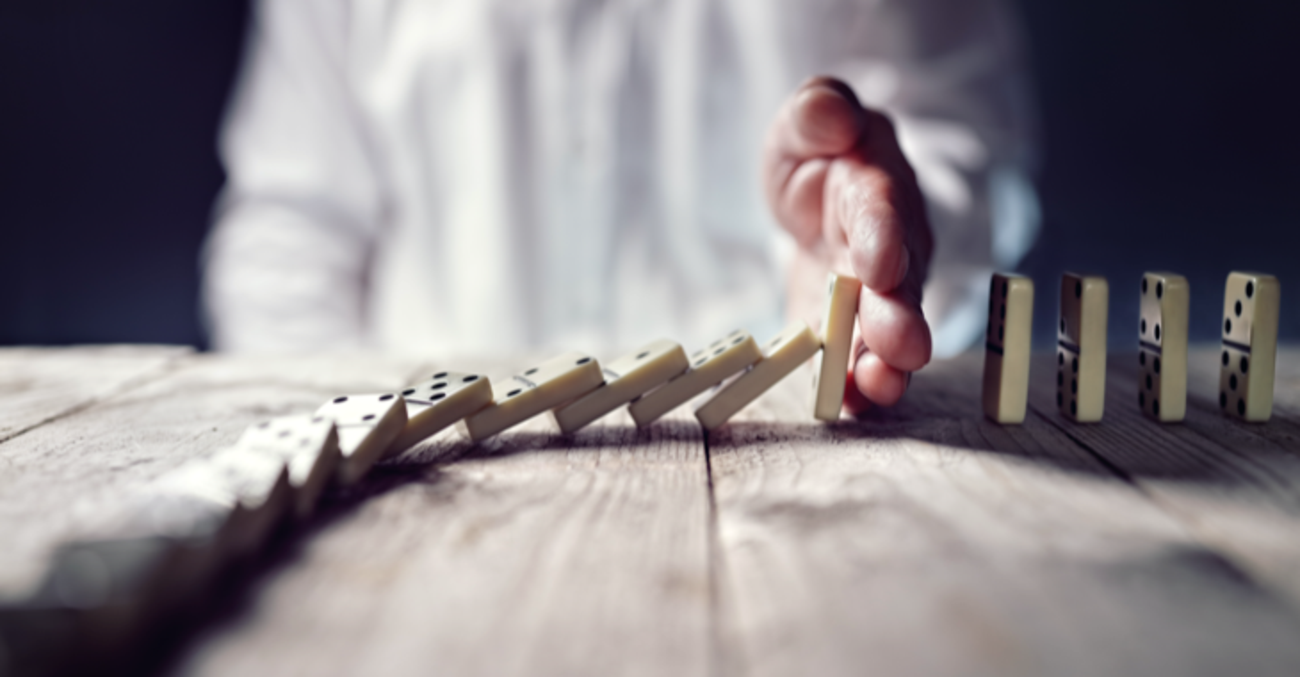 Ein Mann stoppt mit seiner Hand das Umfallen einer Domino-Kette © iStockphoto.com/BrianAJackson Ein Mann stoppt mit seiner Hand das Umfallen einer Domino-Kette © iStockphoto.com/BrianAJackson