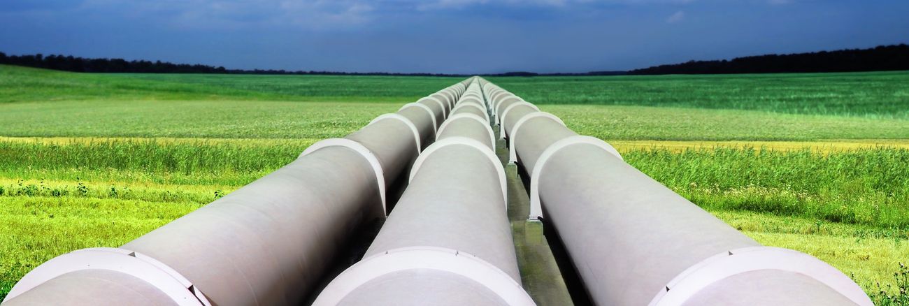 Eine Gaspipeline mit drei riesigen Röhren führt über ein grünes Feld © iStockphoto.com/suaphoto