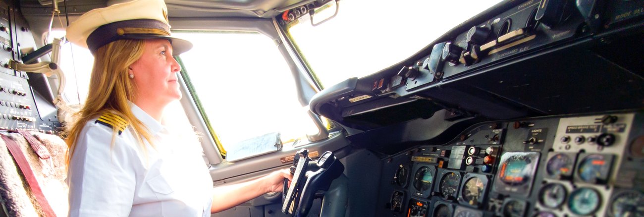Eine Pilotin mit Kapitänsmütze im Cockpit eines © iStock/wsfurlan