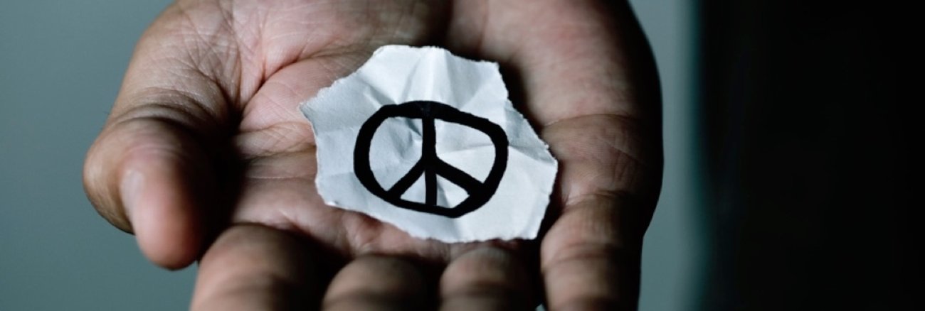 Das CND-Friedenssymbol auf einem abgerissenen Papier in einer aufgehaltenen Hand © iStockphoto.com/nito100
