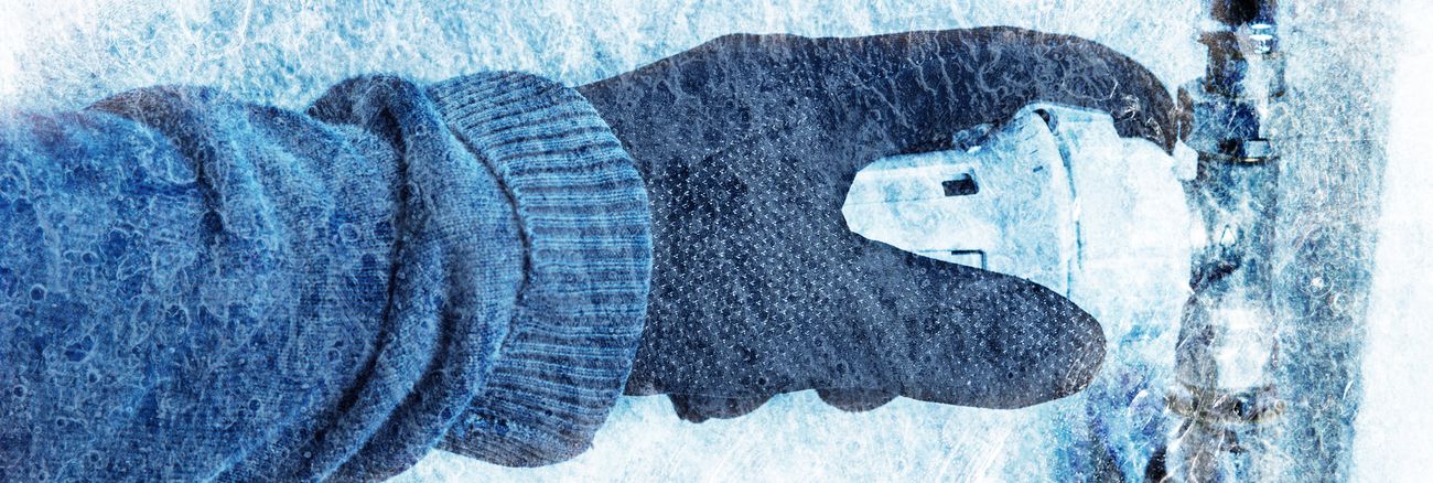 Eine Hand mit Wollhandschuh fasst an den Temperaturregler eines total vereisten Heizkörpers. Foto: © istock.com/BrilliantEye