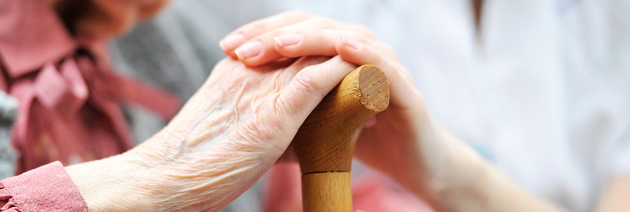 Hand einer Frau auf der Hand einer älteren Frau mit einem Gehstock