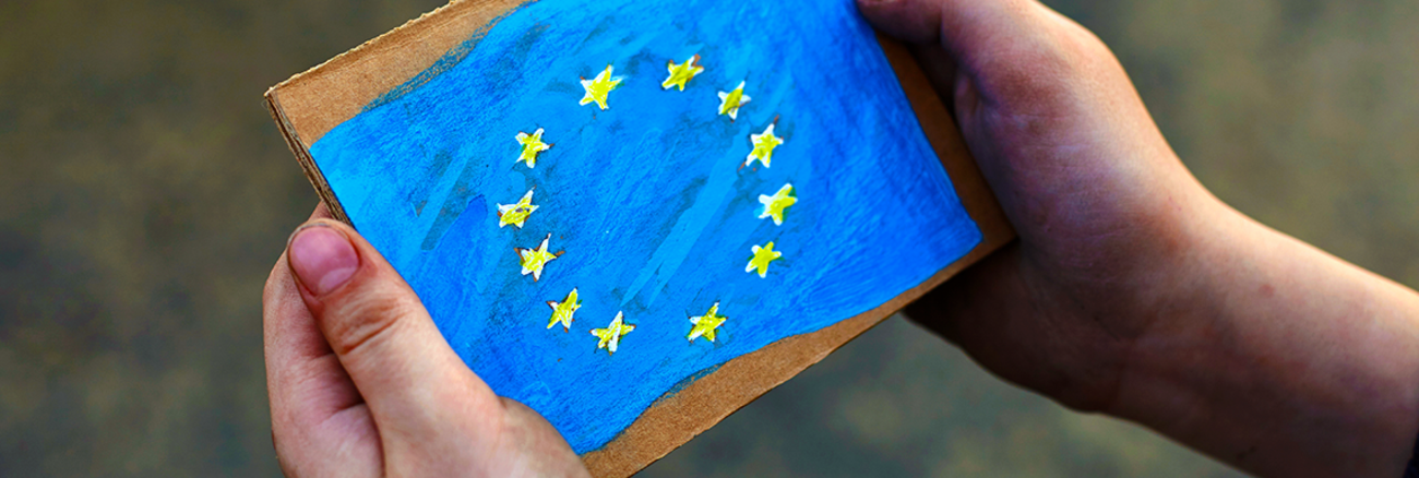 Schmutzige Hände halten Karton mit aufgemalter Europa-Flagge | Foto: © istock.com/bodnarchuk