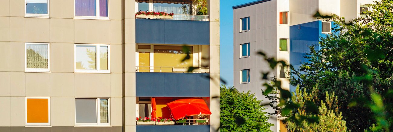 Mehrfamilienhäuser im Plattenbau-Stil mit einem roten Sonnenschirm auf einem Balkon © iStock/deepblue4you