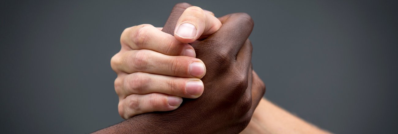 Fester Handschlag zwischen schwarzer und weißer Hand © iStock/JimmyLung