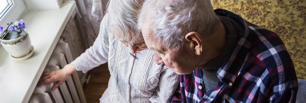 Eine ältere Frau hält eine Rechnung und fasst auf einen Heizkörper, daneben ein älterer Mann mit einer Decke auf den Beinen © iStock/Marina113 Eine ältere Frau hält eine Rechnung und fasst auf einen Heizkörper, daneben ein älterer Mann mit einer Decke auf den Beinen © iStock/Marina113