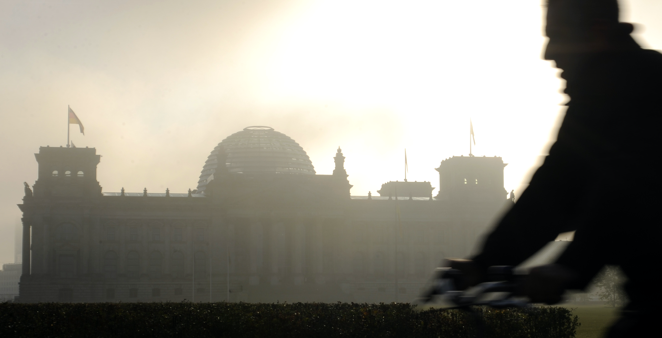 Silhouette eines Fahrradfahrers vor dem Reichstagsgebäude in Morgendunst mit dahinter aufgehender Sonne © picture-alliance/dpa/Rainer Jensen