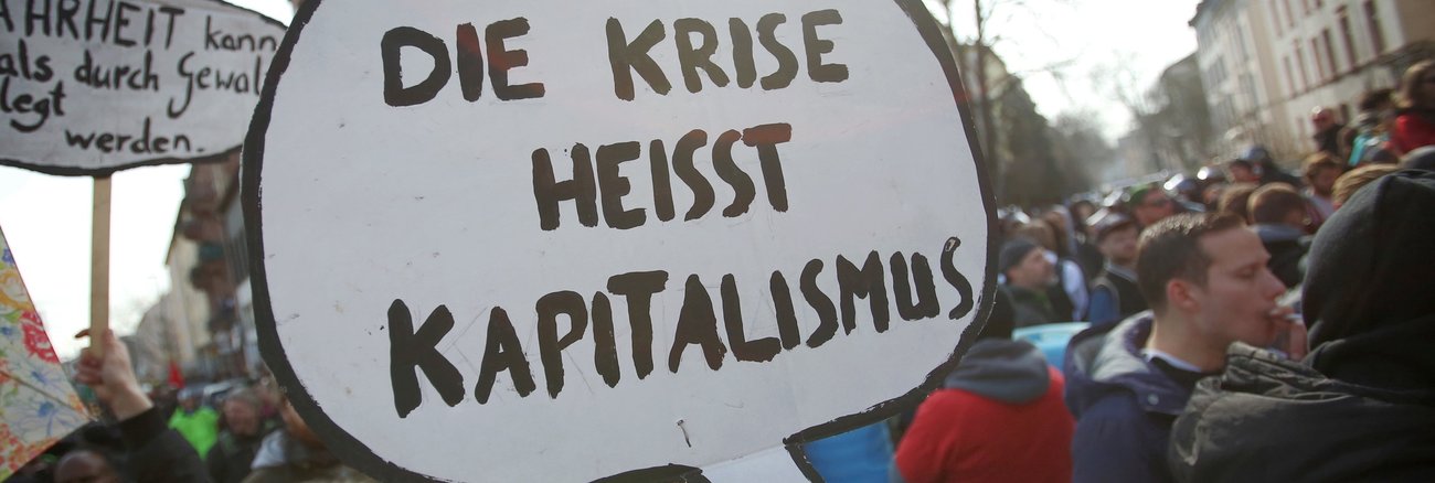 Bei Protesten trägt eine Frau ein Schild mit der Aufschrift »Die Krise heisst Kapitalismus« © Fredrik von Erichsen/dpa