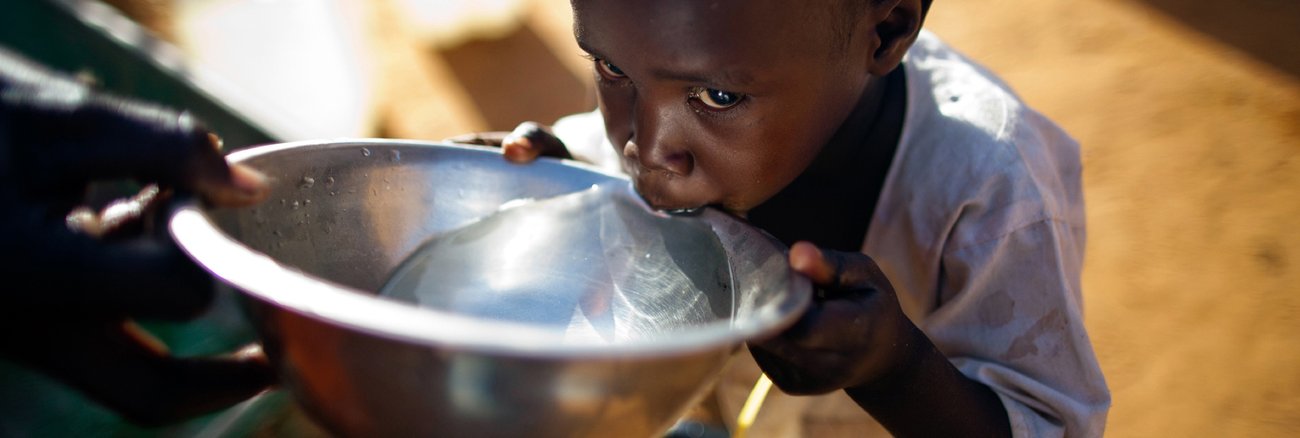 In dem sudaneischen Ort Jebel Saiey reicht ein Vater seinem Sohn eine Metallschale mit Trinkwasser © UN Photo