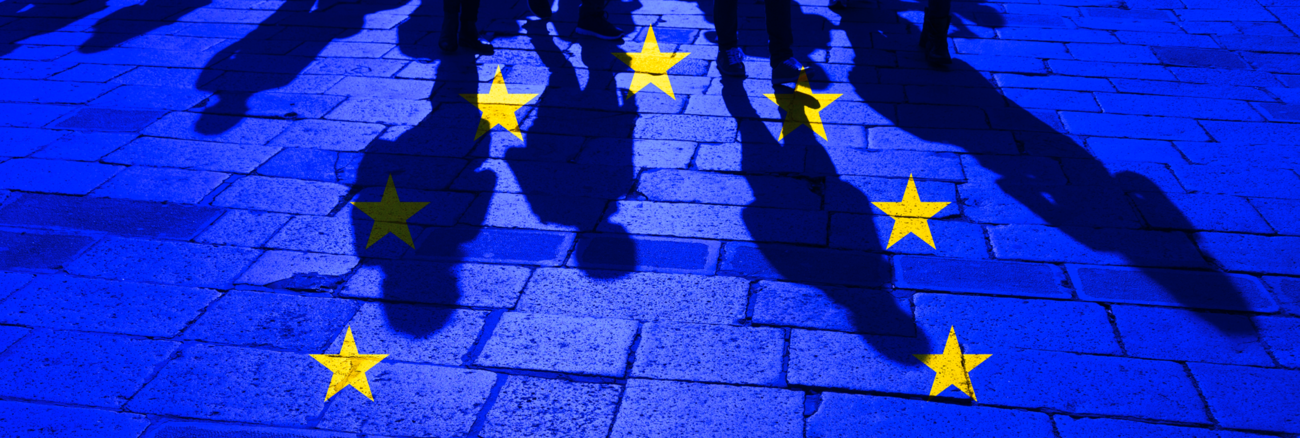 EU-Flagge über Menschenschatten Pflastersteinen © iStock/robertiez