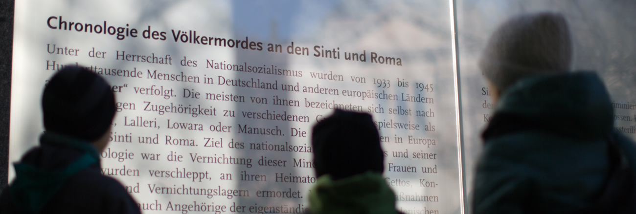 Drei Besucher vor einer Tafel des Denkmals für die vom Nationalsozialismus ermordeten Sinti und Roma in Europa © picture alliance/dpa/Michael Kappeler