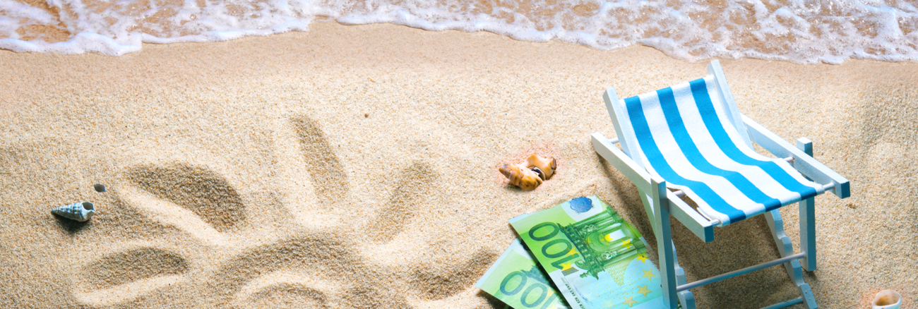 Strand mit Wasser, einer Sonne in den Sand gezeichnet und drei 100-Euro-Scheinen neben einem Liegestuhl © iStock/AlexRaths Strand mit Wasser, einer Sonne in den Sand gezeichnet und drei 100-Euro-Scheinen neben einem Liegestuhl © iStock/AlexRaths