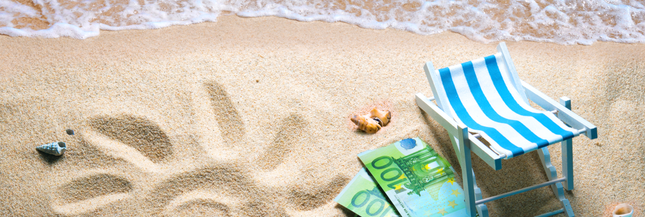 Strand mit Wasser, einer Sonne in den Sand gezeichnet und drei 100-Euro-Scheinen neben einem Liegestuhl © iStock/AlexRaths