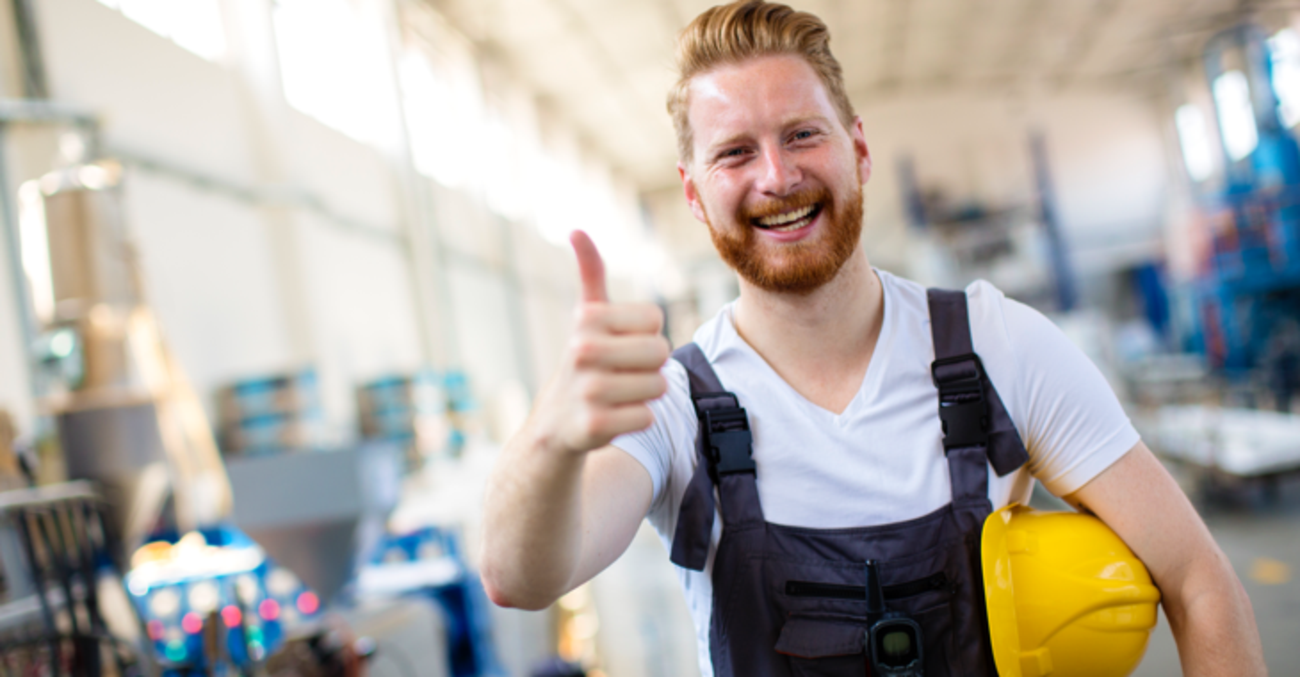 Ein Arbeiter mit gelbem Helm unter seinem linken Arm hebt zustimmend den rechten Daumen © iStock/milanvirijevic