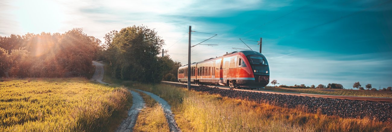 Ein Feldweg neben einem Bahngleis mit einem Regionalexpress der Bahn © iStock/Say-Cheese