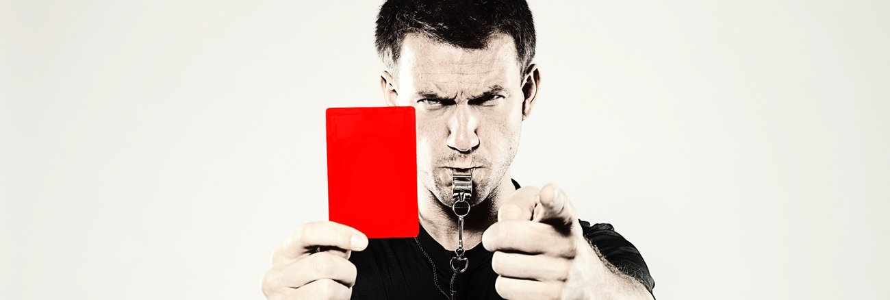 Schiedsrichter mit Pfeife im Mund zeigt die Rote Karte © iStock/decisiveimages