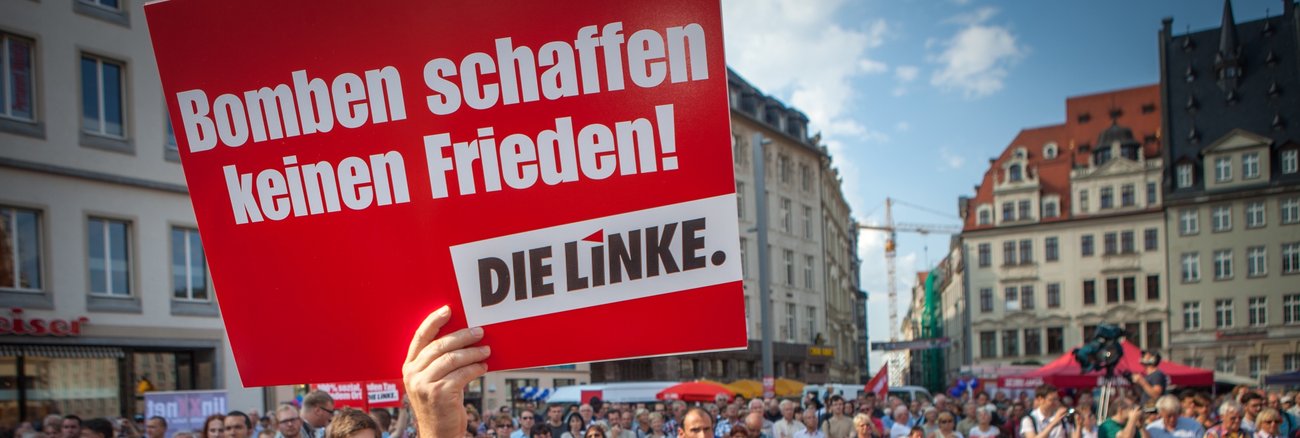 Bei einer Kundgebung in Leipzi hält ein Mann ein Schild mit der Aufschrift »Bomben schaffen keinen Frieden! DIE LINKE« © Jakob Huber