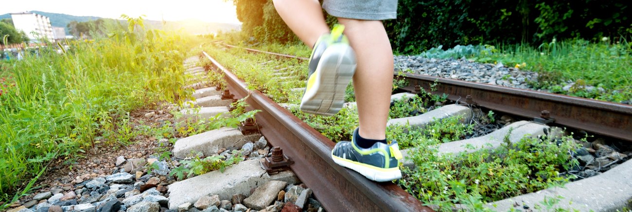 Ein Junge balanciert auf stillgelegten, mit Unkraut bewachsenen Bahngleisen © iStock/baona