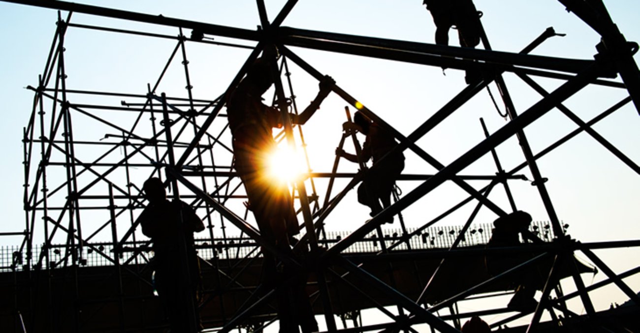 Silhouetten von Bauarbeitern, die auf einer Baustelle Gerüste montieren © iStockphoto.com/hxdbzxy