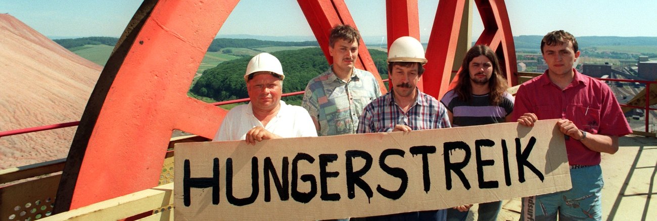 Bergleute halten am 2. Juli 1993 ein Schild mit der Aufschrift Hungerstreik, mit dem sie gegen die von der damaligen Treuhand geplante Schließung der Kaligrube Bischofferode protestieren © dpa/Ralf Hirschberger