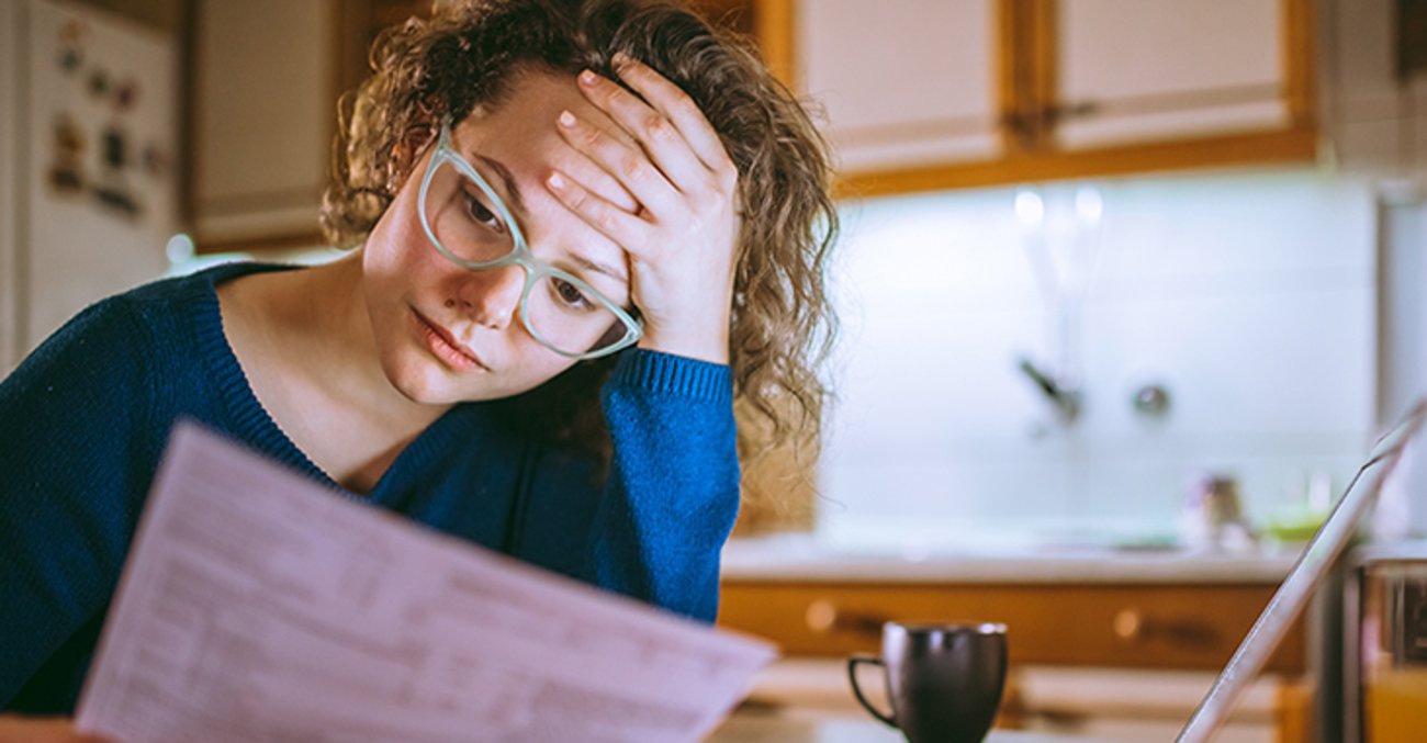Junge Frau am Küchentisch schaut bestürzt auf Schreiben vom Finanzamt 