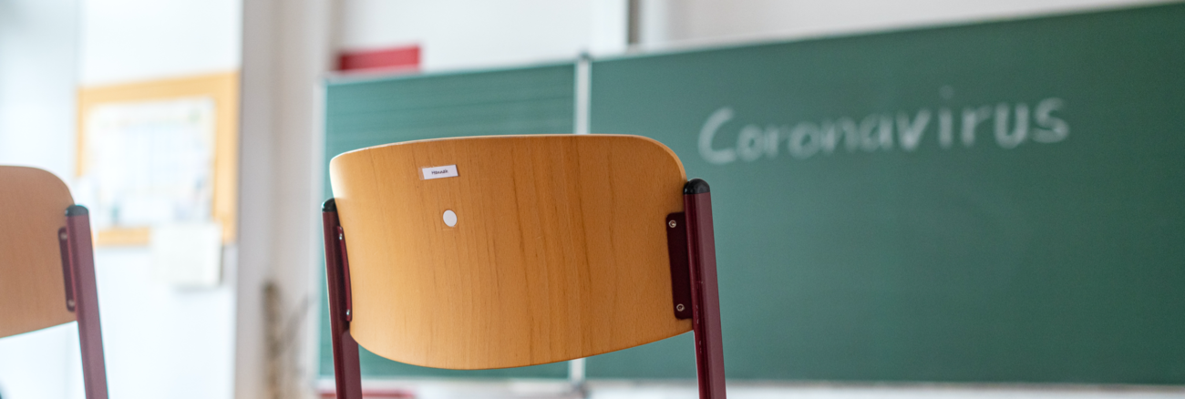 Stühle stehen auf den Tischen in einem leeren Klassenzimmer, an der Tafel steht Coronavirus © dpa/Armin Weigel