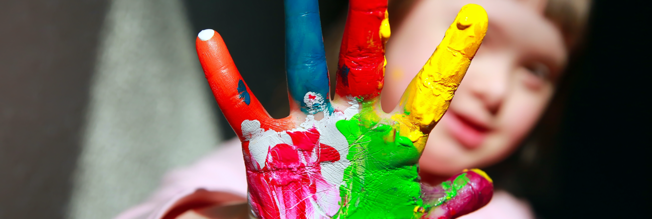Mädchen mit Down-Syndrom hält ihre rechte Hand voller Farbe in die Kamera