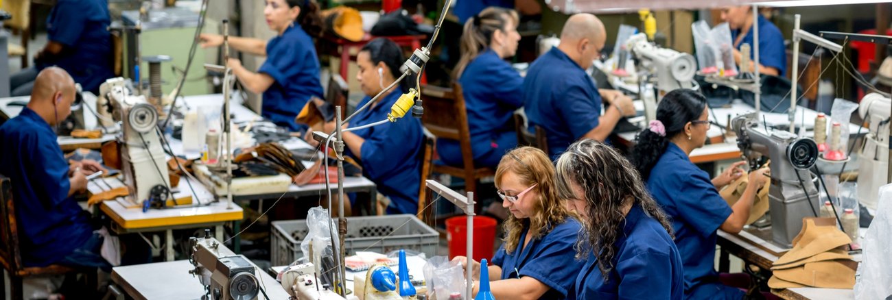 Frauen und Männer in blauen Kitteln arbeiten an Nähmaschinen in einer Fabrik @ iStock/andresr