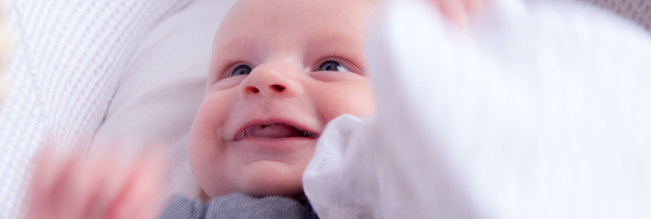 Ein Baby lacht und hällt eine weiße Decke © iStock/TW-Creative
