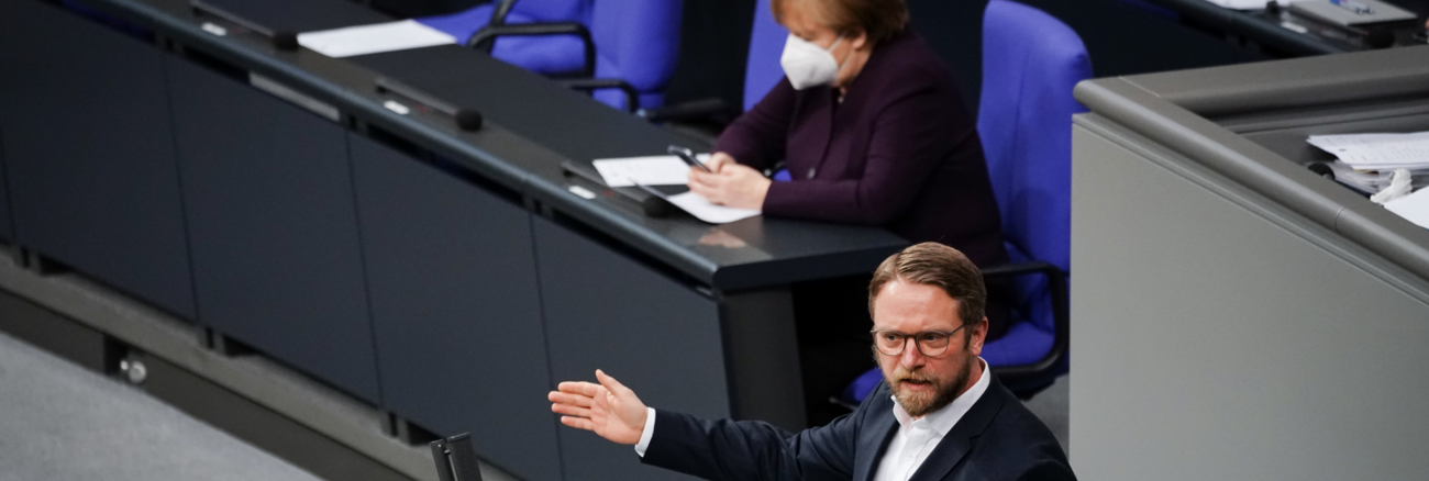 Jan Korte am Rednerpult des Bundestages, dahinter Bundeskanzlerin Merkel auf der Regierungsbank