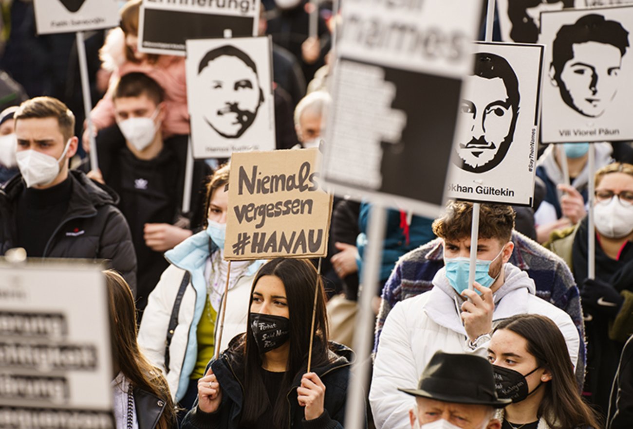 Eine Teilnehmerin hält ein Plakat «niemals vergessen#Hanau» auf der Kundgebung zum Gedenken an den rassistischen Anschlag vor einem Jahr in Hanau. | Foto: © picture alliance/dpa / Andreas Arnold