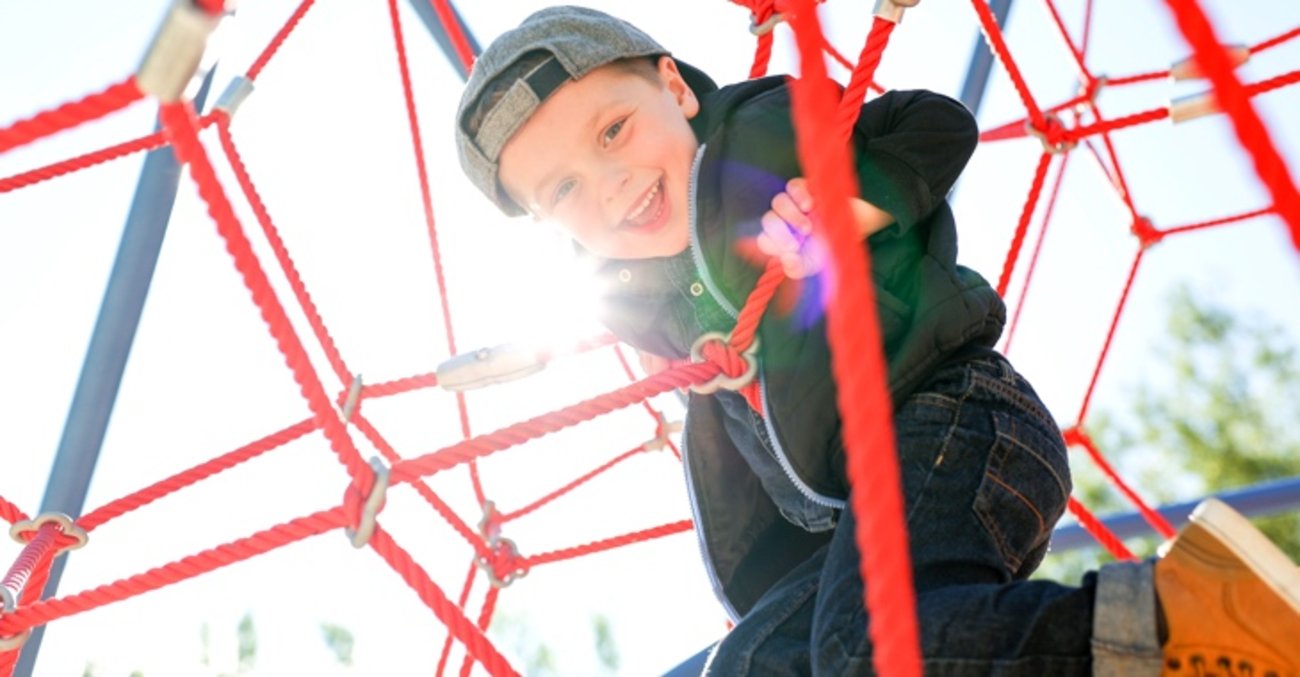Lachender Junge in einem Kletternetz © iStock/LSOphoto