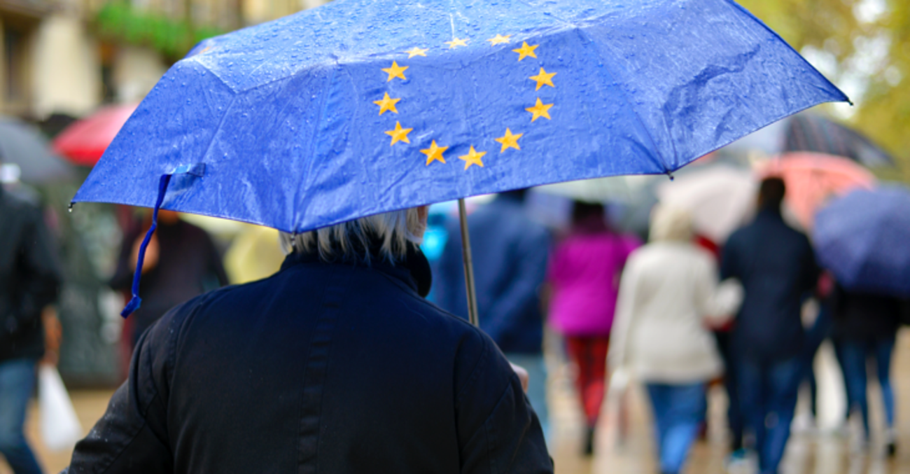 Eine Person hält einen Regenschirm in der Farbe und mit den Sternen der EU-Fahne