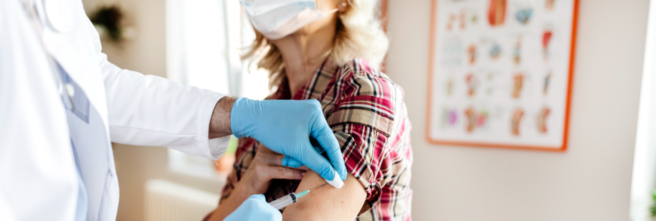 Eine Frau mit Mundschutz wird geimpft © iStock/PixelsEffect