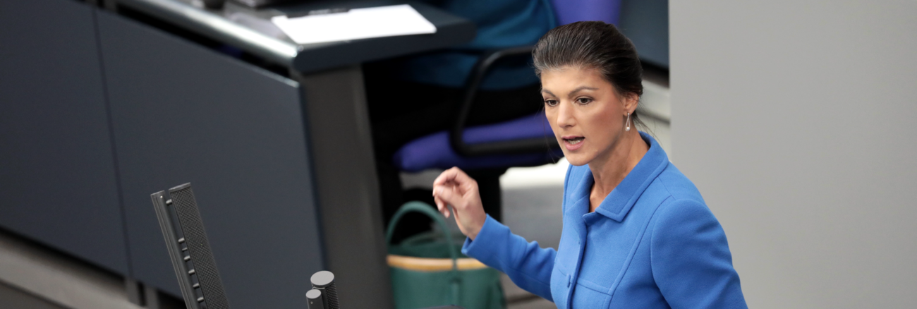 Sahra Wagenknecht am Rednerpult des Bundestages, dahinter Bundeskanzlerin Merkel mit geschlossenen Augen auf der Regierungsbank © picture alliance/dpa/Kay Nietfeld