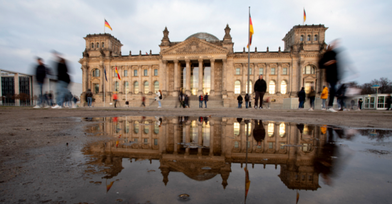 Das Pleargebäude des Bundestages spiegelt sich in einer Pfütze © picture alliance/dpa/Christoph Soeder