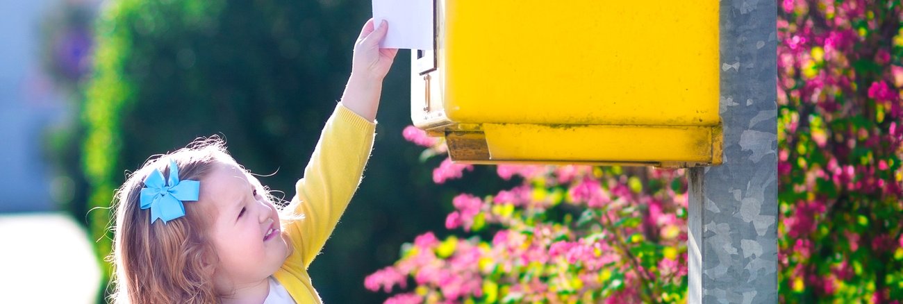 Ein kleines Mädchen steckt mit ausgestrecktem Arm einen Brief in einen Briefkasten © iStock/FamVeld